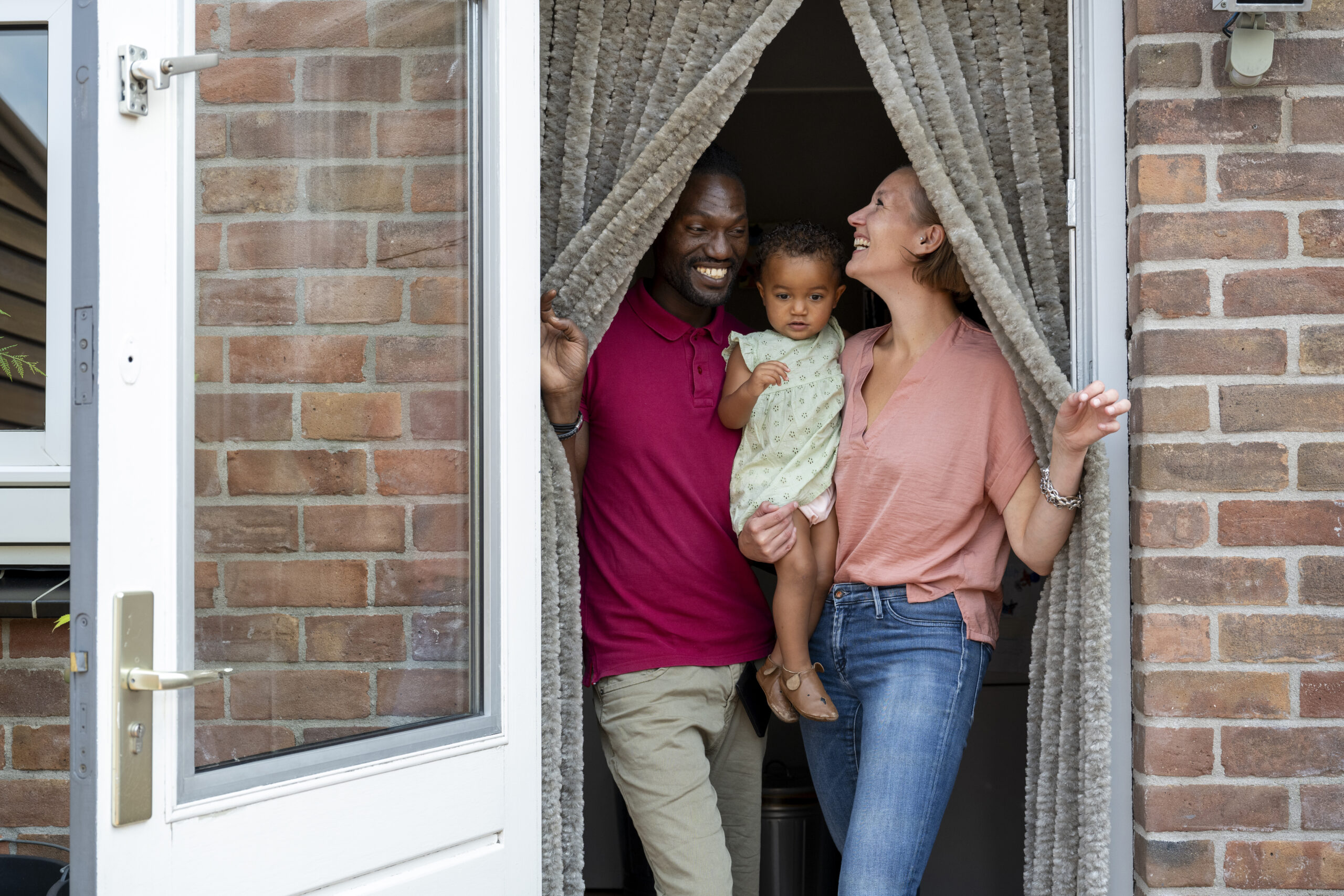 Family smiling and standing at the entrance of their brick home behind an open door.
