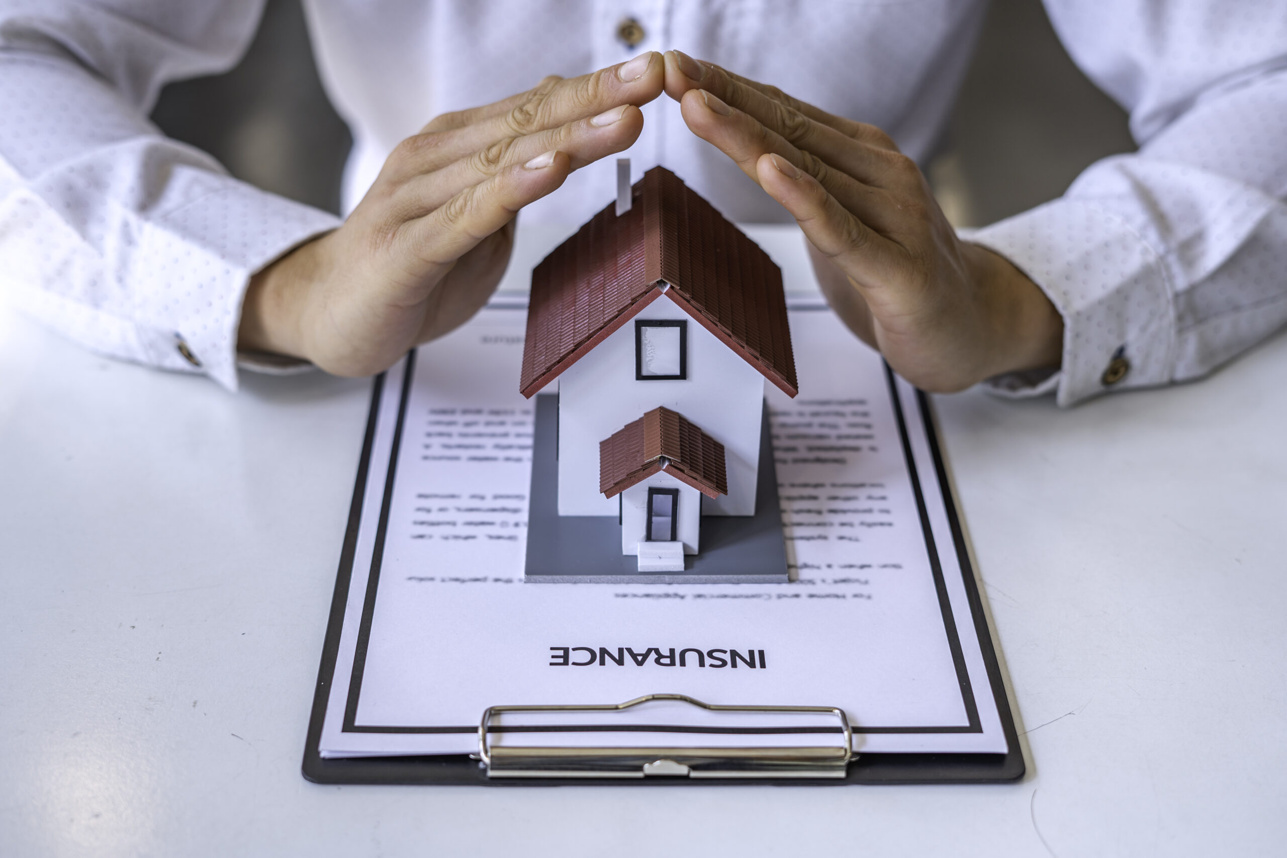 Buildings and Contents insurance concept - A close-up view of a man defending a home model by hand on a table in an office