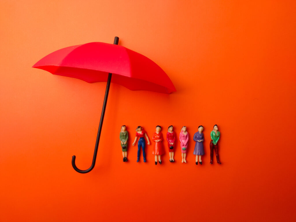 Miniature people women protected by red umbrella of insurance