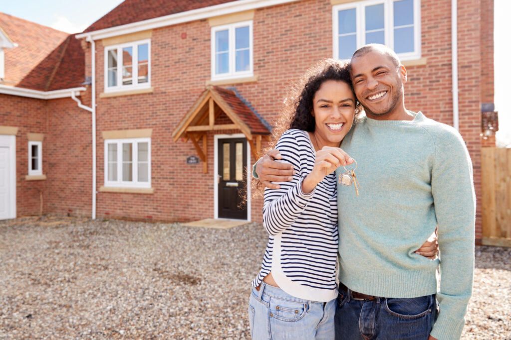 Portrait Of Couple Holding Keys Standing Outside New Home After Smooth Mortgage Process