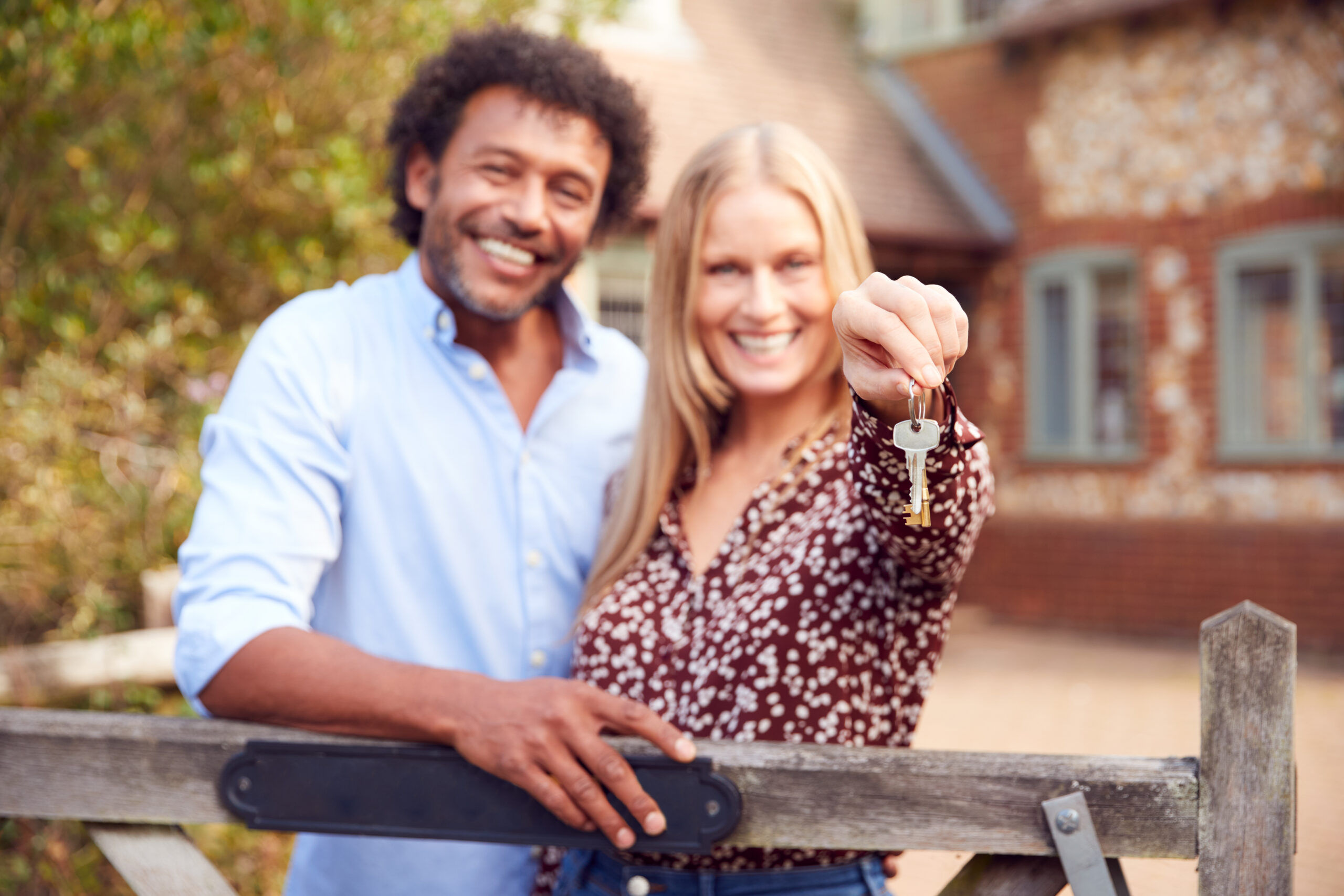 Portrait Of Excited Couple By Gate Holding House Keys Outside New Home following a successful product transfer