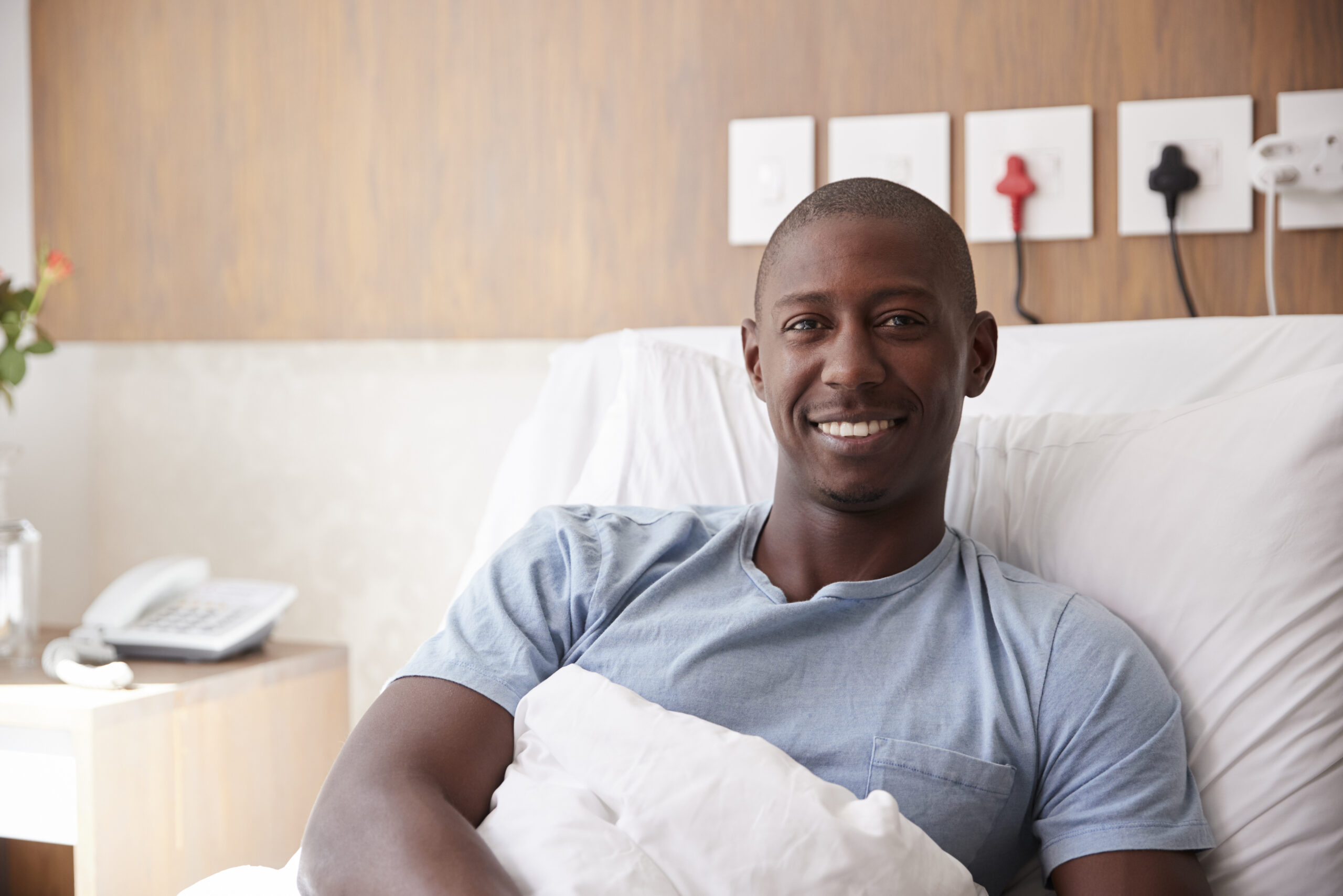 Portrait Of Male Critical Illness Patient Lying In Hospital Bed Smiling At Camera