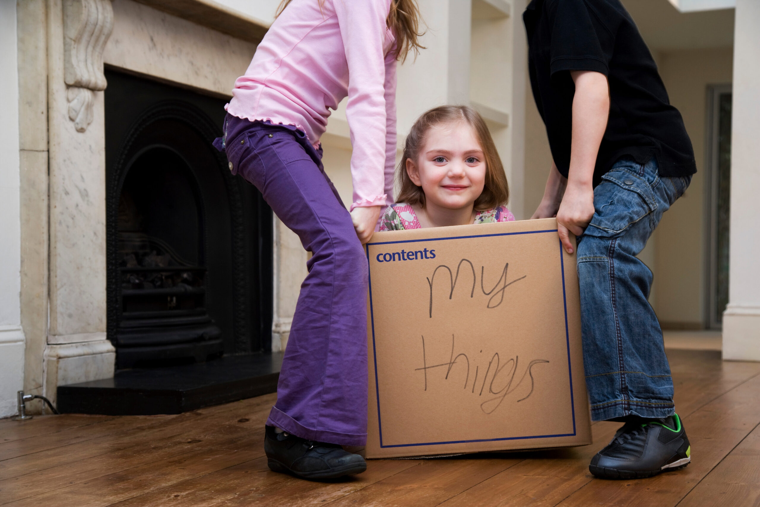 Two children lifting another child in a box reading My things